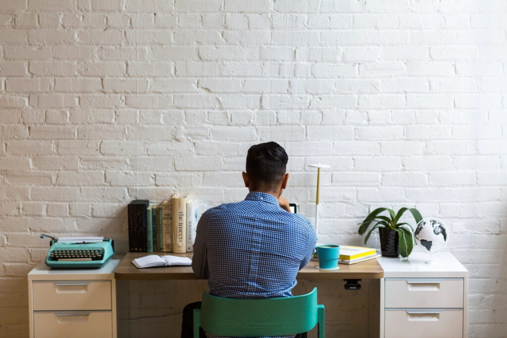 Man working at a desk in a bright office with a white brick wall