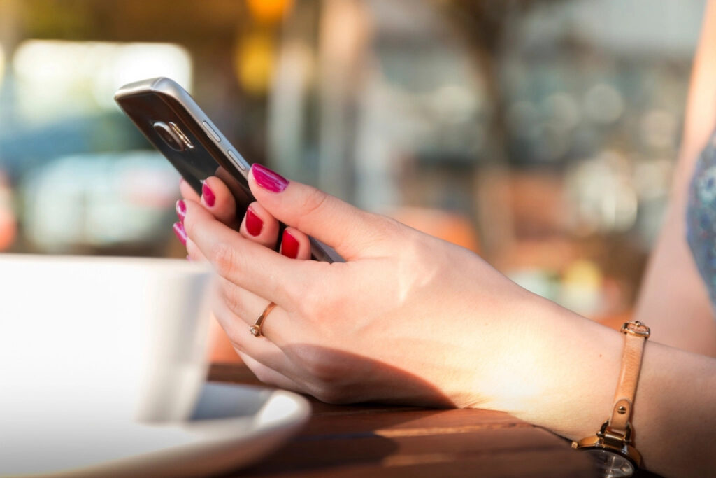 Hands holding a smartphone next to a coffee cup