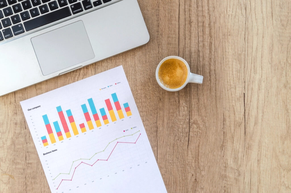 Laptop beside printed sales charts and a cup of coffee