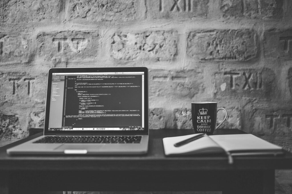 Laptop showing code on a desk against a brick wall